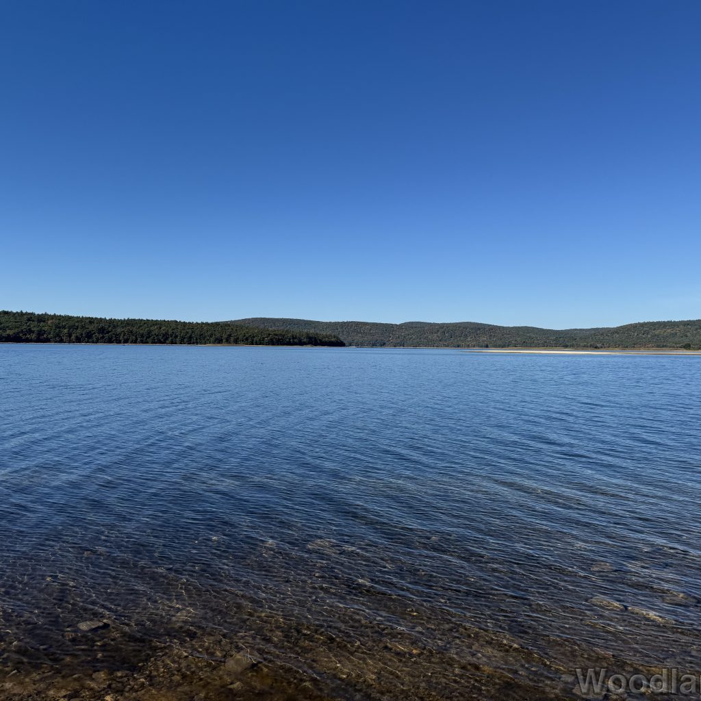 Calm waters of Quabbin Reservoir under a blue sky, with the northern tip of Mount L and ridgeline in the distance