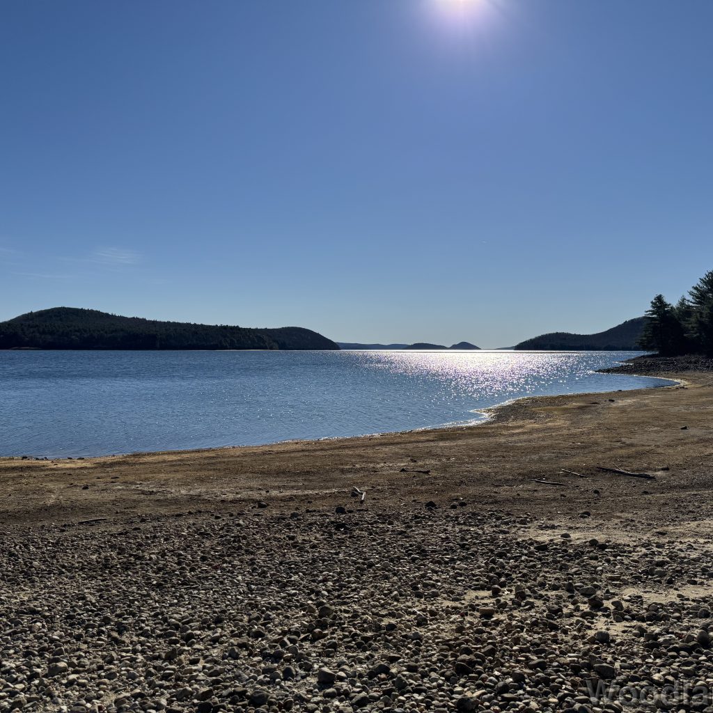 Sunlight shimmering off Quabbin Reservoir under a clear blue sky, distant terrain silhouetted