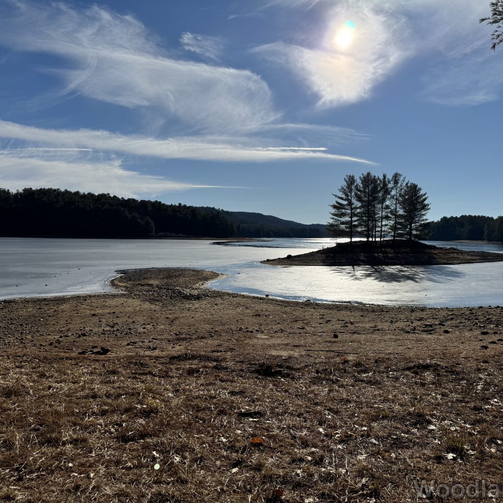 Frozen Quabbin Reservoir under wispy clouds with bright sunlight and a small pine-covered island