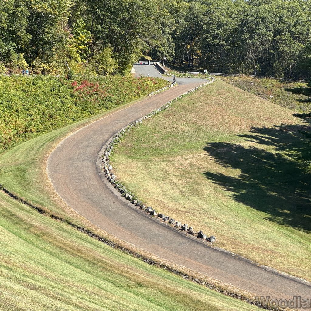 Zoomed-in view of Windsor Dam access road from above the stone wall with green grass and trees