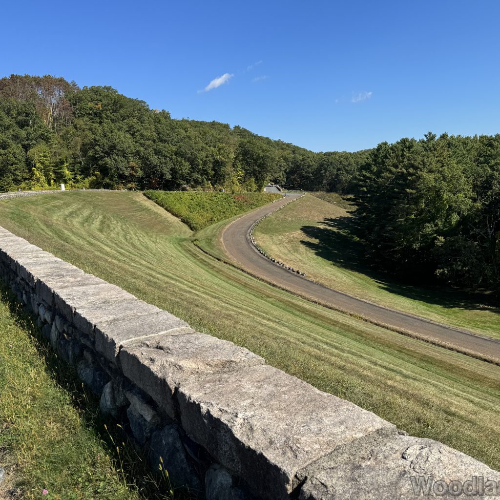 View of Windsor Dam access road from above the stone wall with green grass and trees