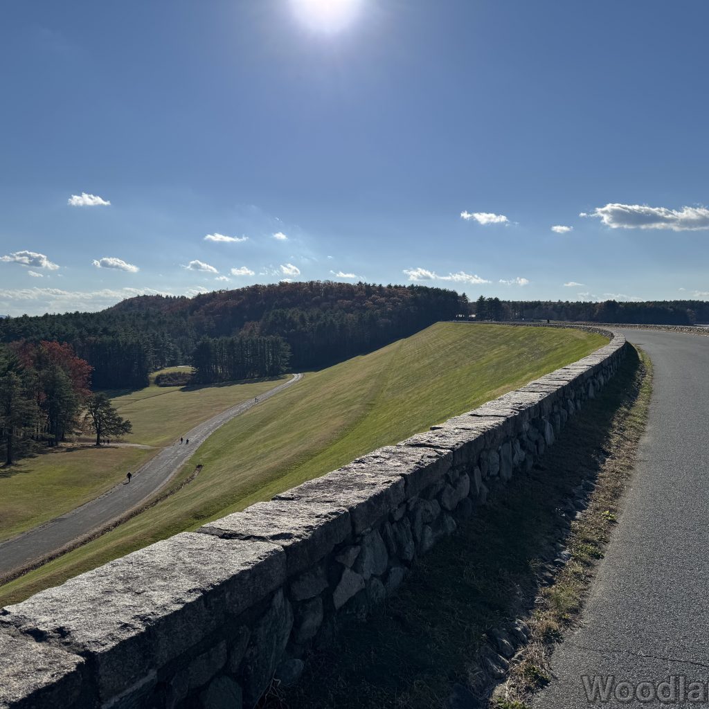 Quabbin Reservoir Windsor Dam grassy slope with access road below and forest in the distance on a bright sunny day