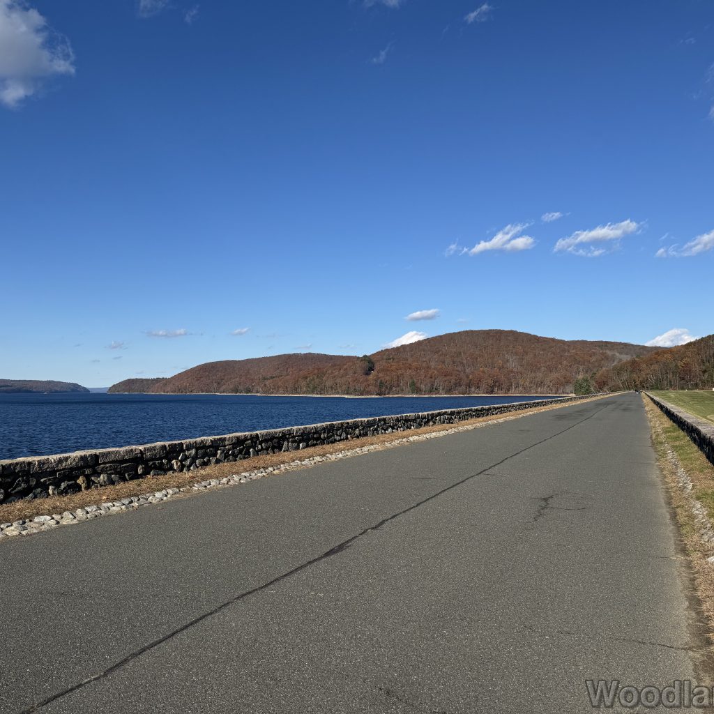 Quabbin Reservoir road atop Windsor Dam facing northeast with distant hills in late November, trees mostly bare without color
