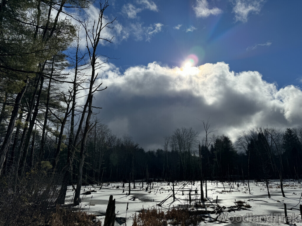 Sun shining from behind a dark cloud above a frozen pond