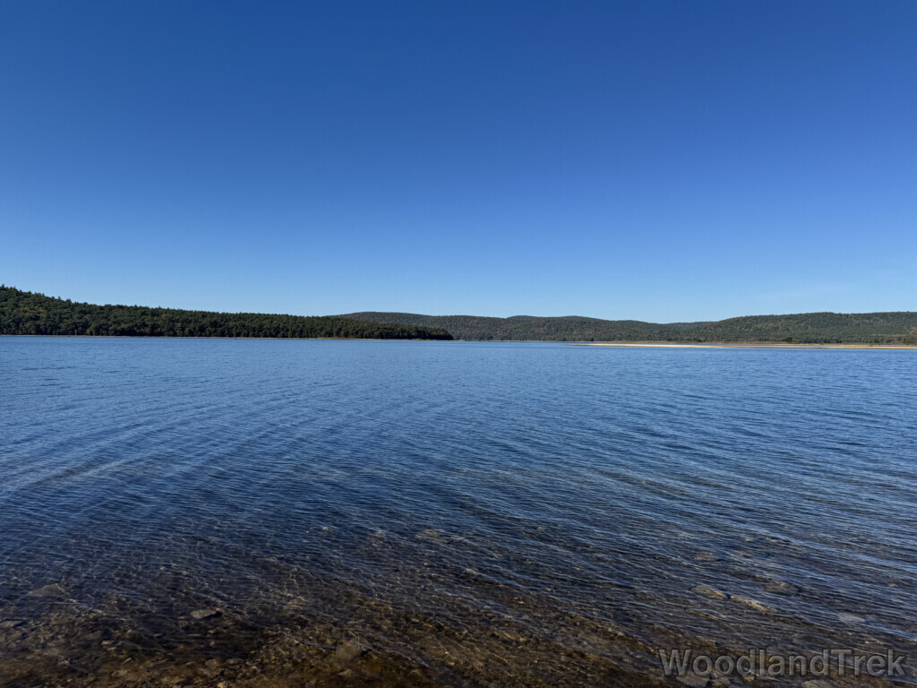 Calm waters of Quabbin Reservoir under a blue sky, with the northern tip of Mount L and ridgeline in the distance
