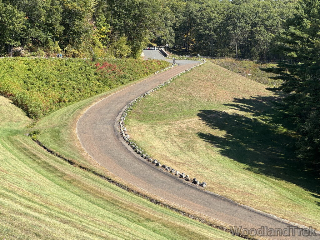 Zoomed-in view of Windsor Dam access road from above the stone wall with green grass and trees