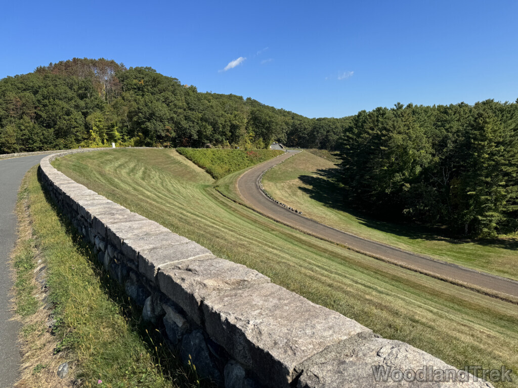 View of Windsor Dam access road from above the stone wall with green grass and trees